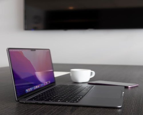 A laptop closed next to a small ceramic cup on a wooden dining table indicating the end of a remote workday